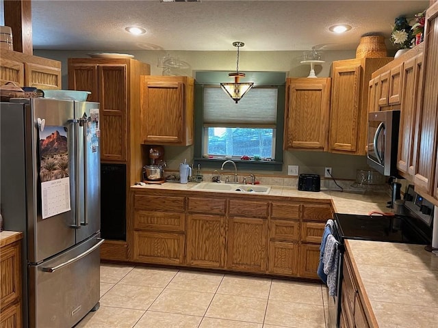 kitchen featuring stainless steel appliances, tile countertops, pendant lighting, sink, and a textured ceiling