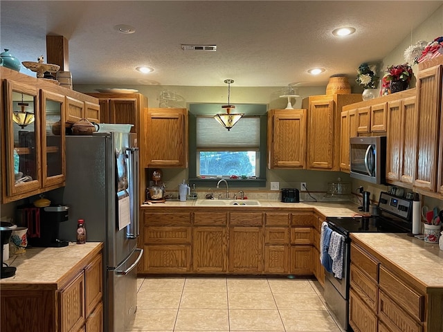 kitchen with light tile patterned floors, a textured ceiling, stainless steel appliances, hanging light fixtures, and sink