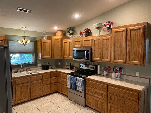 kitchen featuring decorative light fixtures, stainless steel appliances, sink, tile counters, and light tile patterned floors