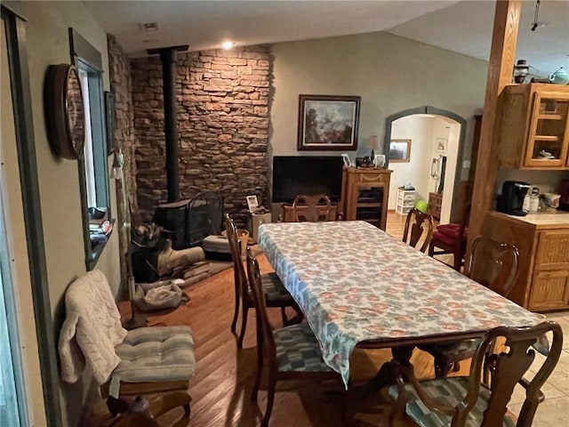 dining space with light wood-type flooring, lofted ceiling, and a wood stove