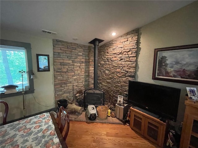 living room with vaulted ceiling, a wood stove, and light hardwood / wood-style flooring