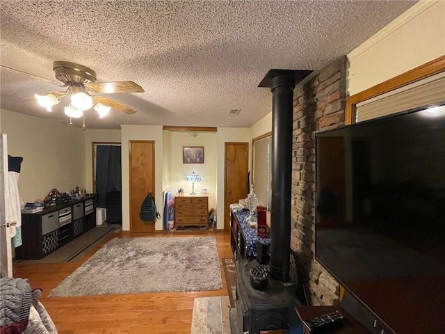 living room featuring hardwood / wood-style flooring, a wood stove, a textured ceiling, and ceiling fan