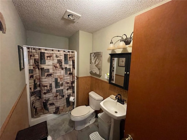 bathroom with a shower with shower curtain, toilet, sink, and a textured ceiling