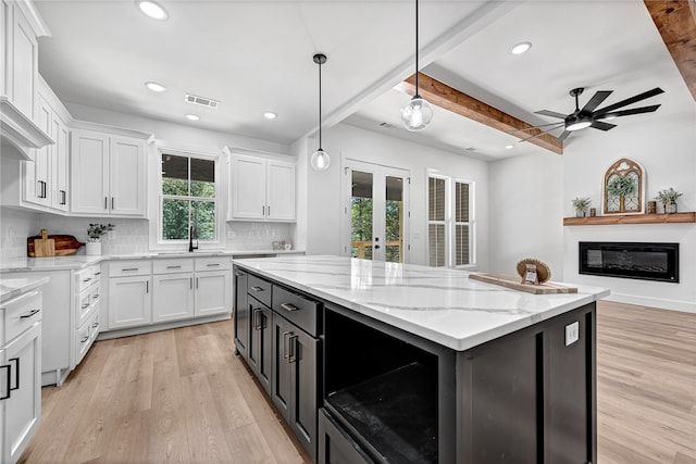 kitchen featuring white cabinets, hanging light fixtures, tasteful backsplash, beamed ceiling, and light hardwood / wood-style flooring