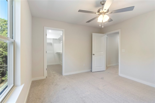 unfurnished bedroom featuring light carpet, a spacious closet, a closet, and ceiling fan