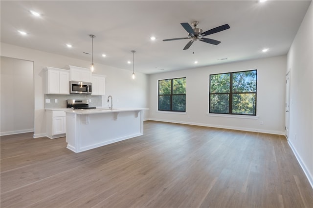 kitchen with sink, white cabinetry, appliances with stainless steel finishes, pendant lighting, and a kitchen island with sink