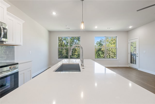 kitchen with sink, white cabinetry, appliances with stainless steel finishes, pendant lighting, and backsplash