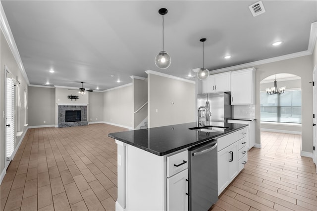 kitchen featuring a healthy amount of sunlight, ceiling fan with notable chandelier, a brick fireplace, an island with sink, and light hardwood / wood-style floors