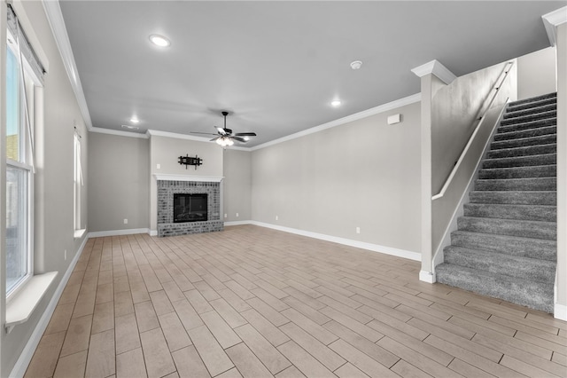 unfurnished living room featuring ceiling fan, a wealth of natural light, crown molding, and a brick fireplace