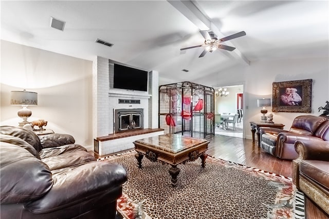 living room featuring lofted ceiling with beams, a fireplace, ceiling fan with notable chandelier, brick wall, and hardwood / wood-style flooring