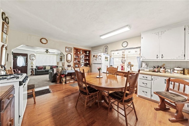 dining space featuring light wood-style floors, arched walkways, ceiling fan, and a textured ceiling