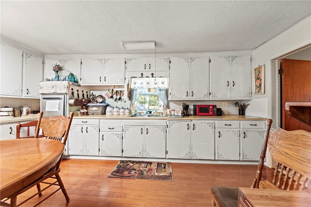 kitchen featuring white cabinets, decorative backsplash, a textured ceiling, and light hardwood / wood-style flooring