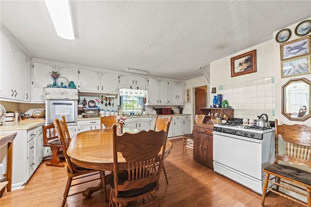 kitchen featuring light countertops, decorative backsplash, light wood-style floors, white cabinetry, and white range with gas cooktop