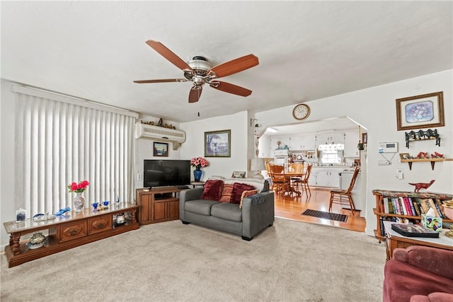 living room featuring carpet, arched walkways, ceiling fan, and a wall mounted air conditioner