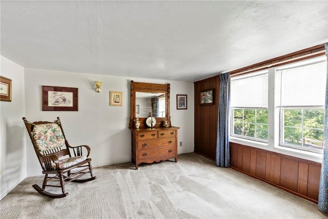 sitting room featuring light colored carpet, wood walls, and a textured ceiling