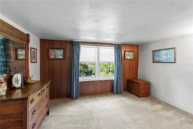 unfurnished bedroom with a textured ceiling, wood walls, and light colored carpet