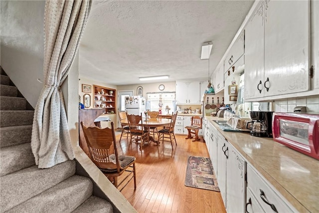 kitchen with a textured ceiling, white cabinetry, light wood-style floors, light countertops, and freestanding refrigerator