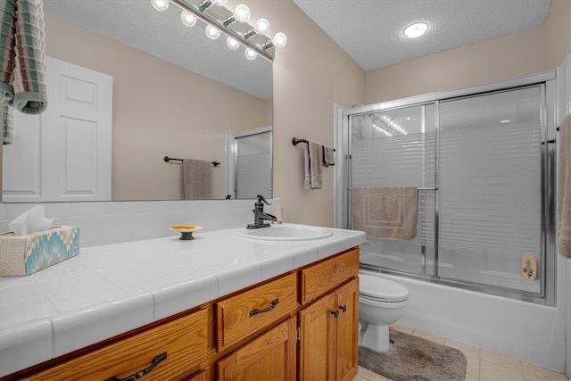 full bathroom featuring vanity, shower / bath combination with glass door, toilet, a textured ceiling, and tile patterned flooring