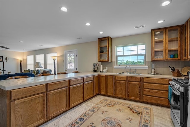 kitchen with tasteful backsplash, sink, kitchen peninsula, light tile patterned floors, and stainless steel gas range oven