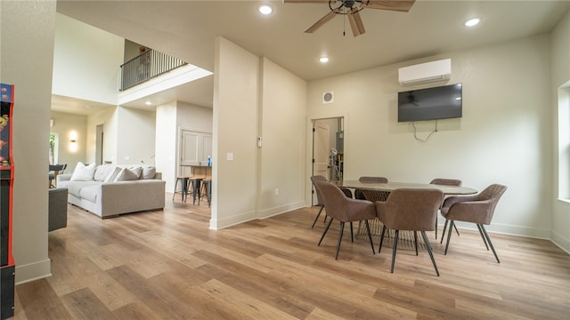 dining area with ceiling fan, light hardwood / wood-style floors, a wall unit AC, and a high ceiling