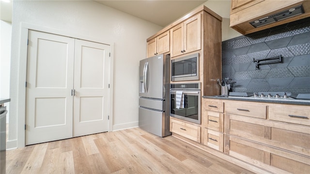 kitchen featuring stainless steel appliances, premium range hood, light brown cabinetry, and light wood-type flooring