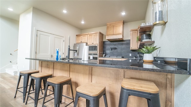 kitchen with dark stone countertops, light brown cabinets, light hardwood / wood-style floors, appliances with stainless steel finishes, and decorative backsplash