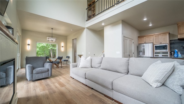 living room featuring an inviting chandelier, light wood-type flooring, and a towering ceiling