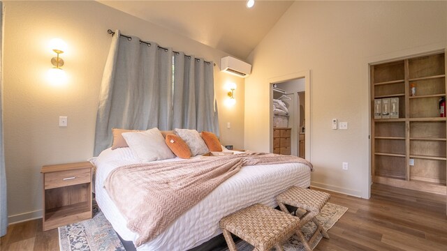 bedroom featuring a spacious closet, high vaulted ceiling, a wall mounted AC, and wood-type flooring