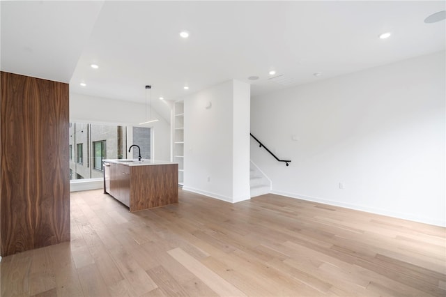 unfurnished living room featuring recessed lighting, light wood-style floors, a sink, baseboards, and stairs