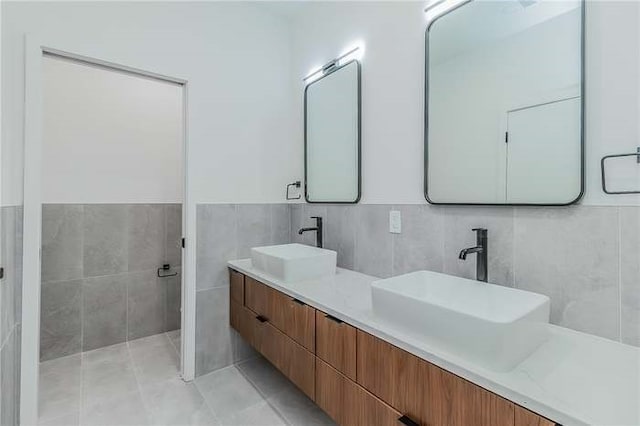 bathroom with tile patterned flooring, a sink, tile walls, and double vanity