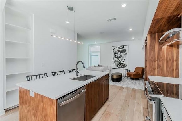 kitchen with sink, pendant lighting, light hardwood / wood-style floors, a center island with sink, and appliances with stainless steel finishes