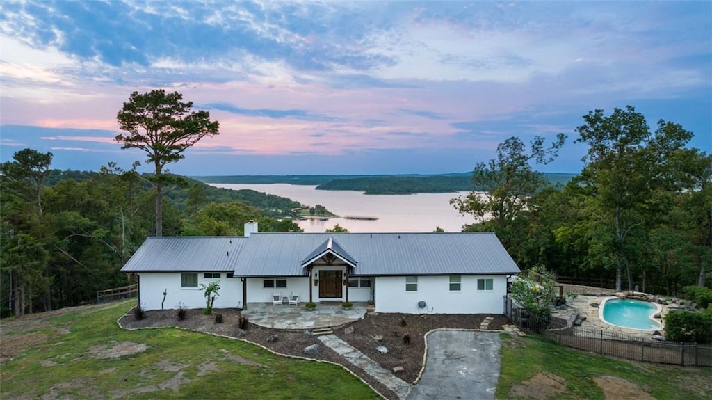 view of front facade featuring a fenced in pool, a patio, a water view, and a yard