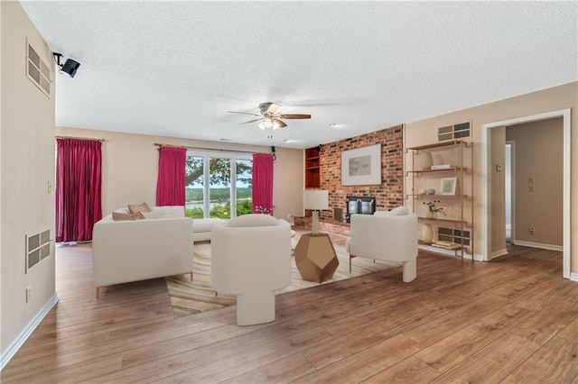 living room featuring ceiling fan, wood-type flooring, a textured ceiling, and a brick fireplace