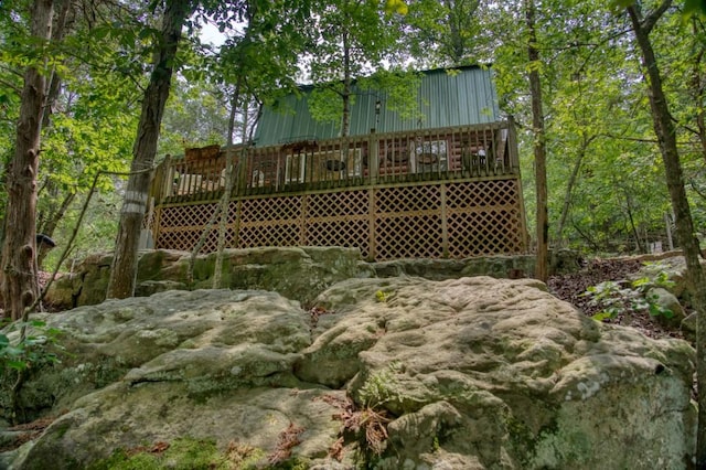 rear view of house with metal roof, a wooden deck, and a forest view
