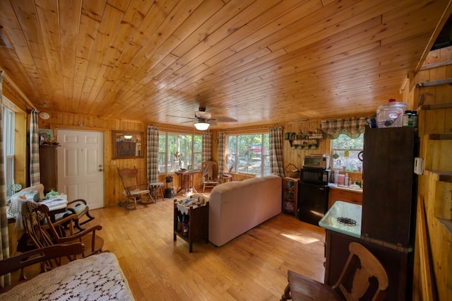 living room featuring light hardwood / wood-style floors, wooden walls, a wealth of natural light, and ceiling fan