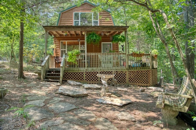 exterior space featuring a forest view, faux log siding, a gambrel roof, and a porch