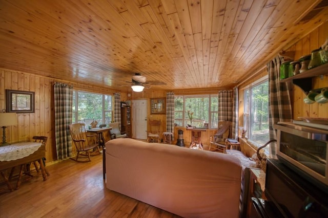 living area featuring a ceiling fan, light wood-style flooring, wooden ceiling, and wood walls