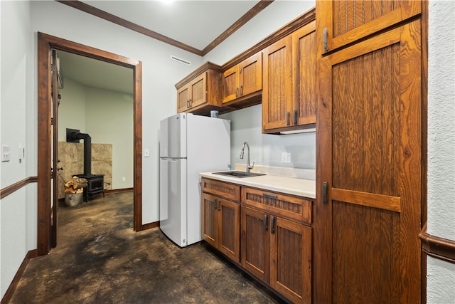 kitchen with white refrigerator, sink, ornamental molding, and a wood stove