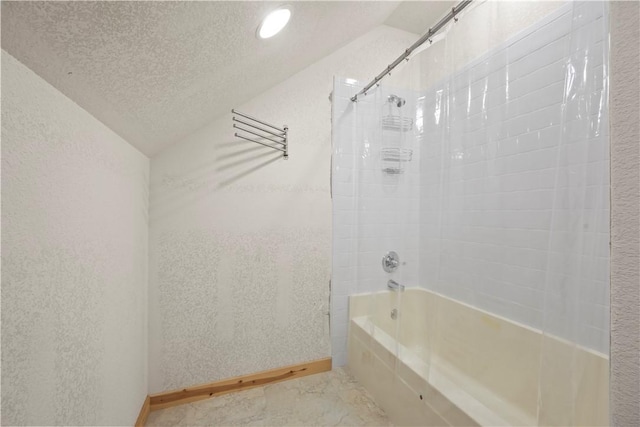 bathroom with vaulted ceiling, a textured ceiling, washtub / shower combination, a textured wall, and baseboards