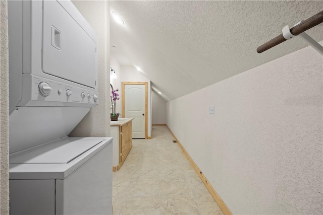 clothes washing area featuring a textured ceiling, baseboards, stacked washer and clothes dryer, a textured wall, and laundry area