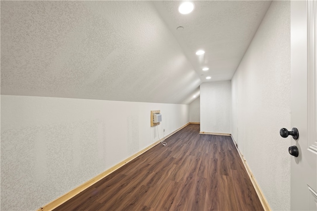 bonus room with vaulted ceiling, a textured ceiling, a wall mounted air conditioner, and dark hardwood / wood-style flooring