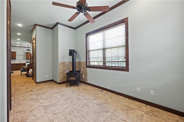 empty room with ceiling fan, ornamental molding, and a wood stove