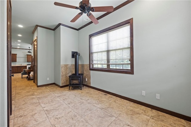 empty room featuring baseboards, recessed lighting, a ceiling fan, crown molding, and a wood stove