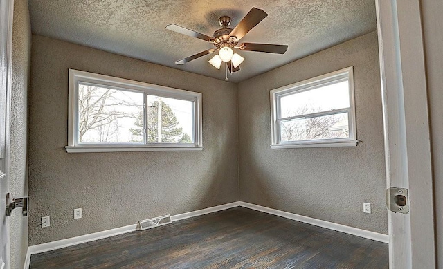 spare room featuring a textured ceiling, dark wood-type flooring, and a healthy amount of sunlight