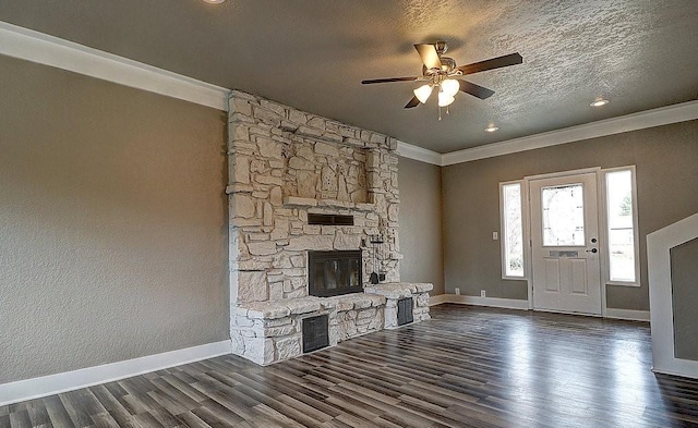 unfurnished living room with a stone fireplace, crown molding, a textured ceiling, dark hardwood / wood-style floors, and ceiling fan