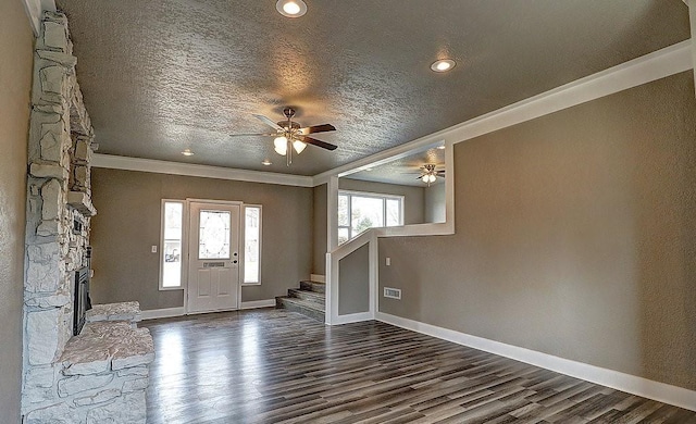 entryway with crown molding, a stone fireplace, a textured ceiling, and dark hardwood / wood-style flooring