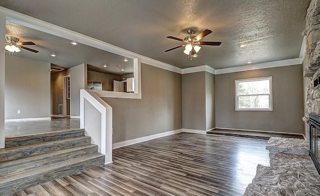 unfurnished living room with crown molding, ceiling fan, a fireplace, a textured ceiling, and dark hardwood / wood-style flooring