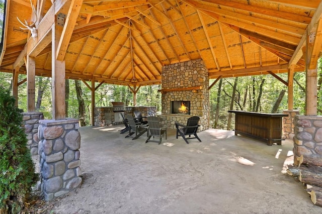 view of patio / terrace featuring a bar, a gazebo, an outdoor stone fireplace, and exterior kitchen