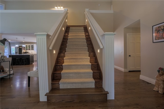 stairs with ornate columns, wood-type flooring, and a high ceiling