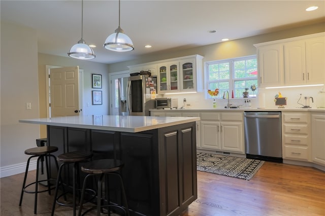 kitchen with light wood-type flooring, appliances with stainless steel finishes, sink, white cabinets, and a center island